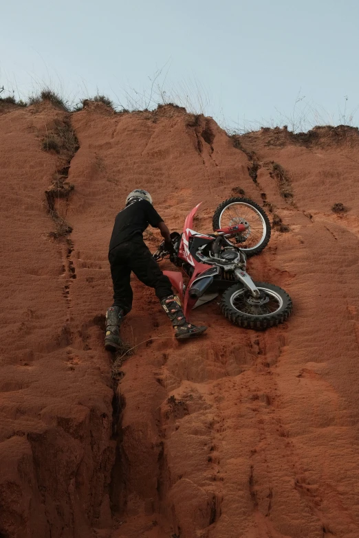 a man climbs up the side of a steep hill with his bike