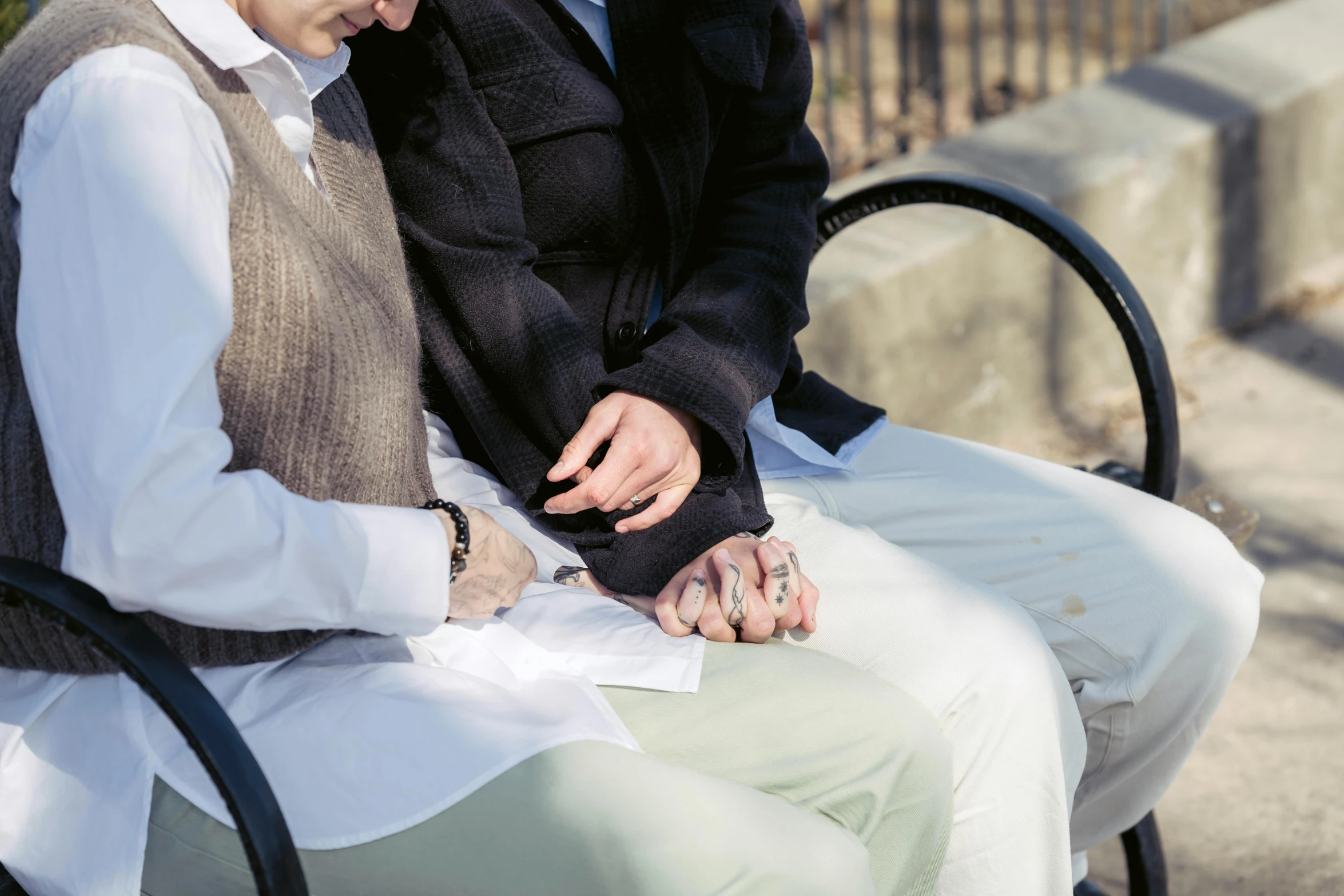 two men sit on a bench touching hands