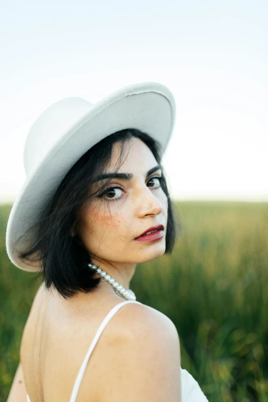 a woman in a hat is sitting in the middle of the grass