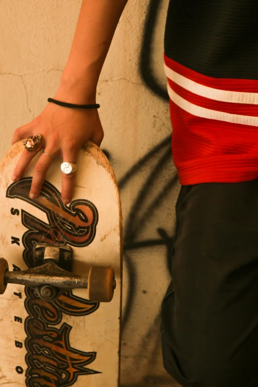 a hand holding onto a skateboard in front of a wall