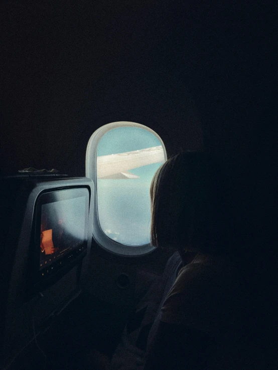 an airplane window shows an airplane wing and sky in the dark