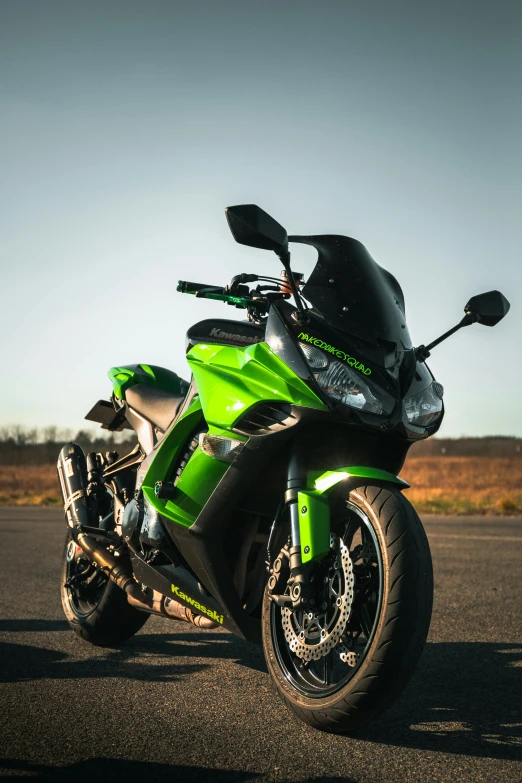 a green motorcycle parked on a road next to a grass field