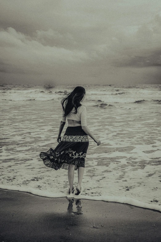 black and white image of girl on beach in flowing dress with ocean in background