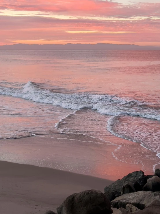 an ocean view with rocks and pink clouds