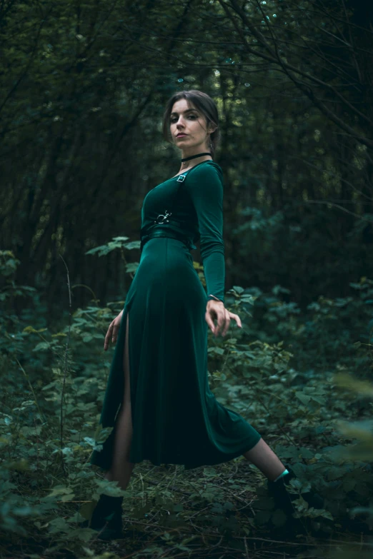 a woman is standing in the woods wearing a green dress