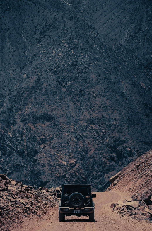 a jeep drives along a road near a mountainous hill