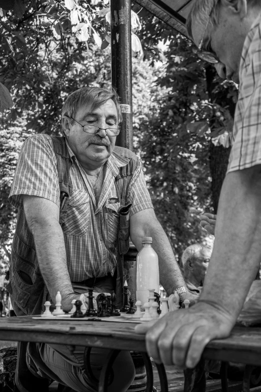 black and white pograph of two men playing chess under an umbrella