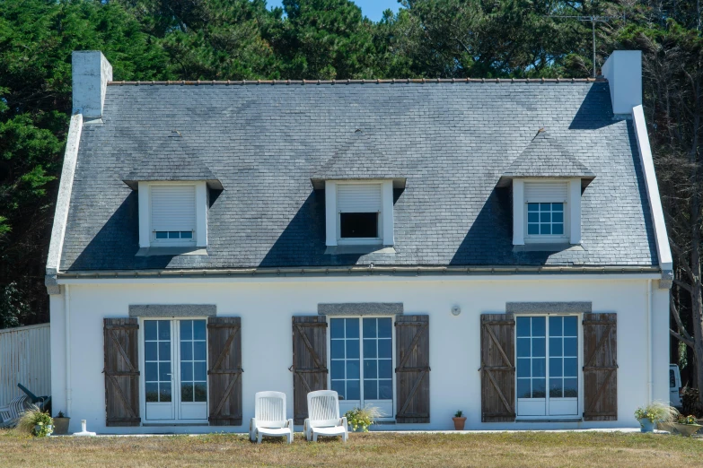 there is a house with brown shutters and two chairs in front