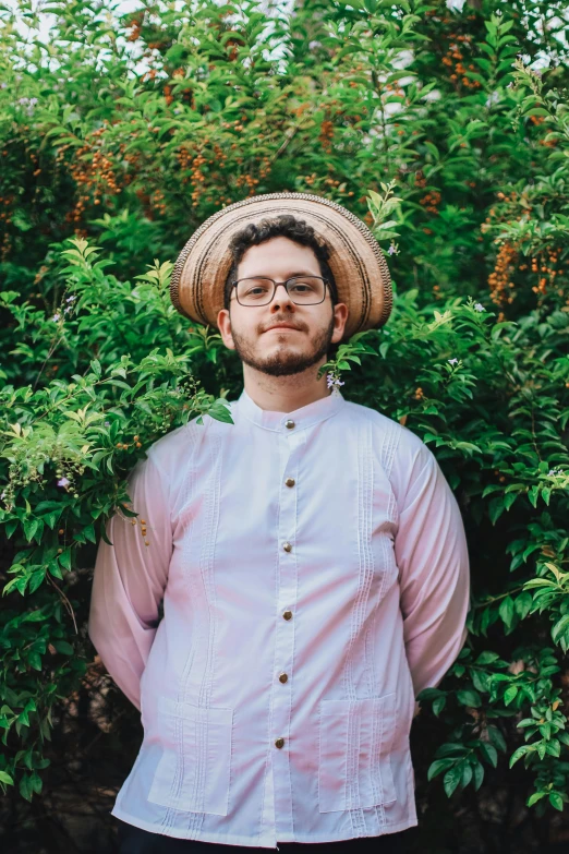 a man standing in front of shrubbery in a straw hat