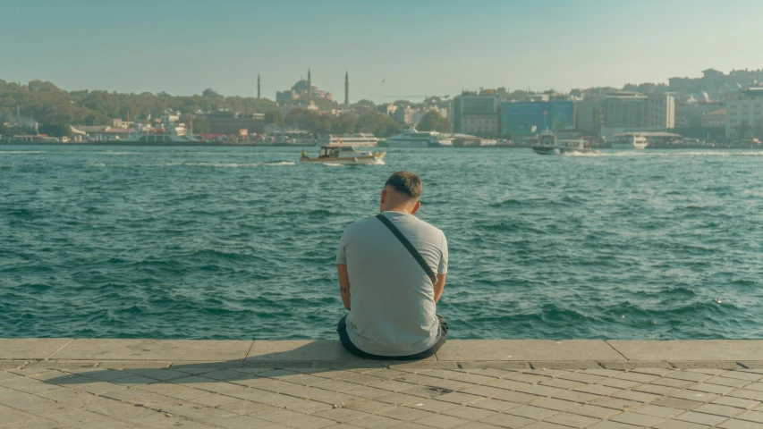 a man sitting on the edge of the river looking at the city