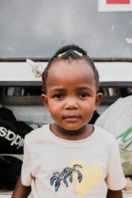 a black little girl in a white shirt stands in front of a truck