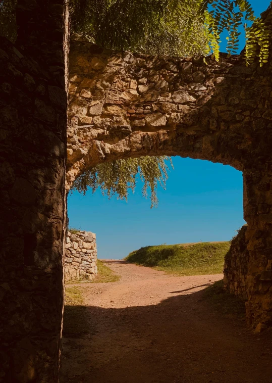 a dirt path near an old stone wall under a blue sky