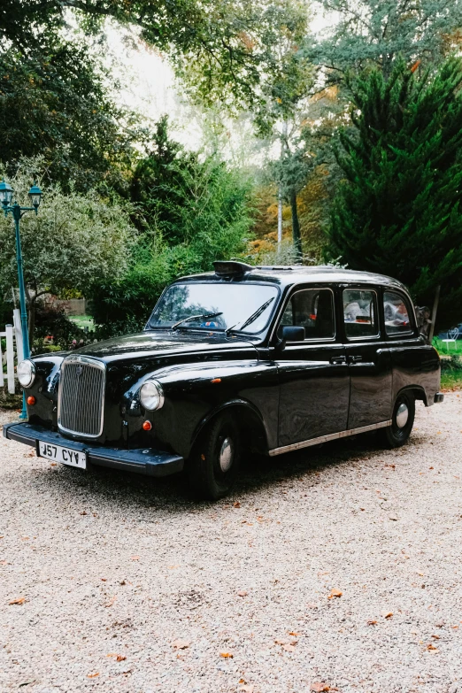 a black vintage car sits on gravel next to some trees