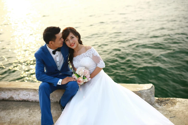 a bride and groom are seated on the edge of the water