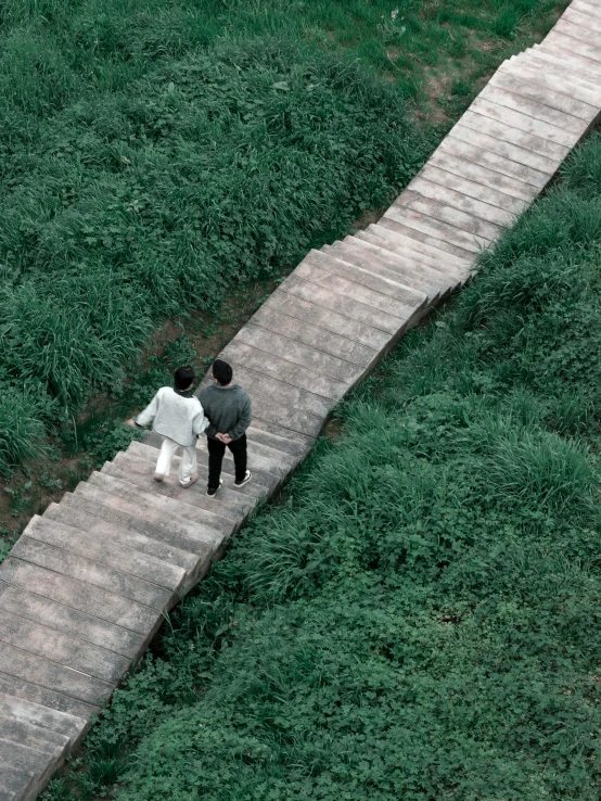 two people are walking up a pathway between grassy area