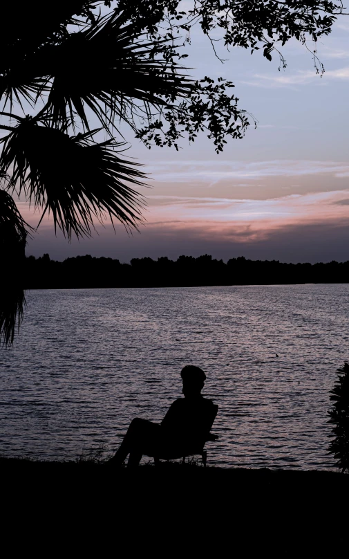 man sitting on a bench watching sunset over a lake
