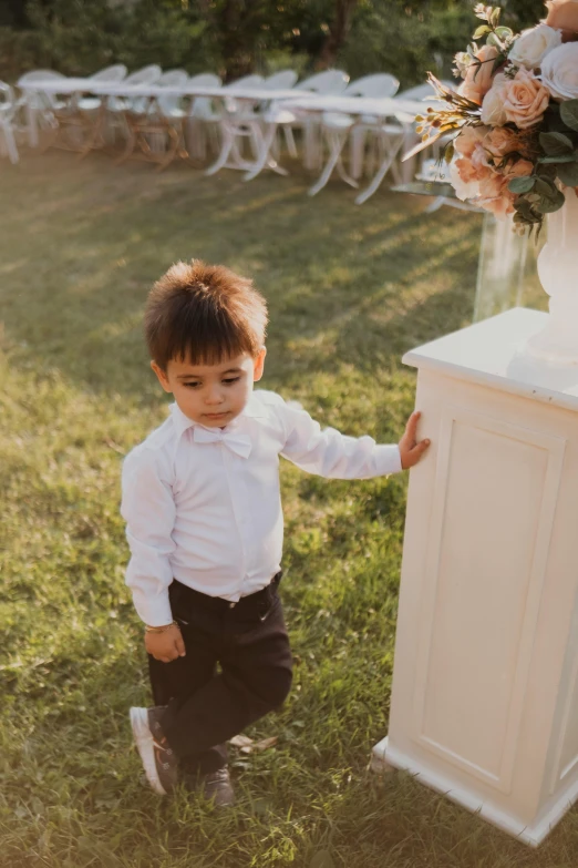 a boy in white shirt and black pants next to an old chair with a flower