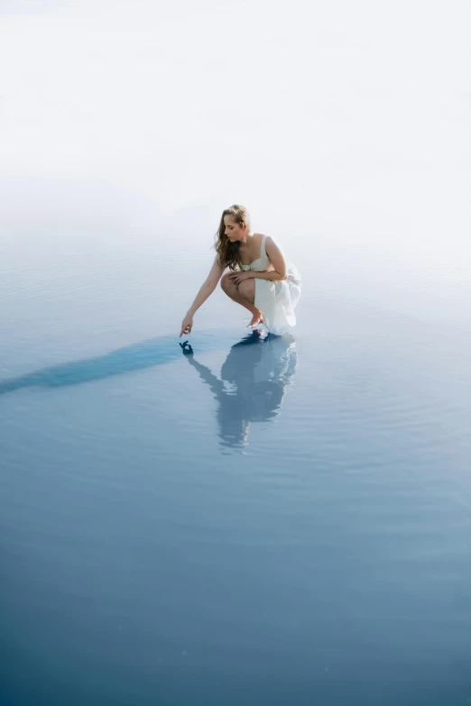 a woman kneeling in water next to a blue wave