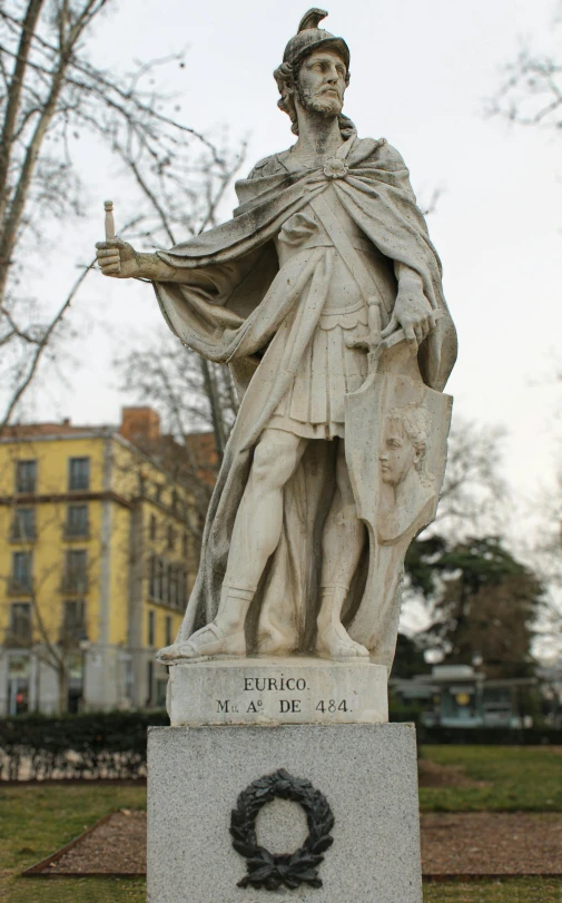 statue standing on sidewalk in city area next to bushes