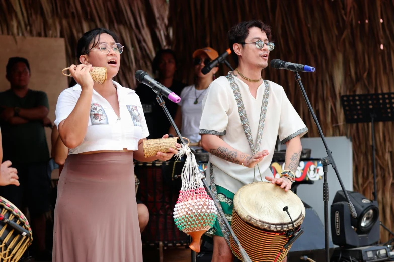 two women perform on stage, one in a skirt and the other holding a bag