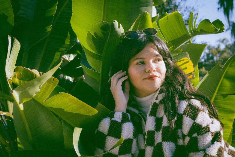 a woman standing by a bunch of plants while talking on a cell phone