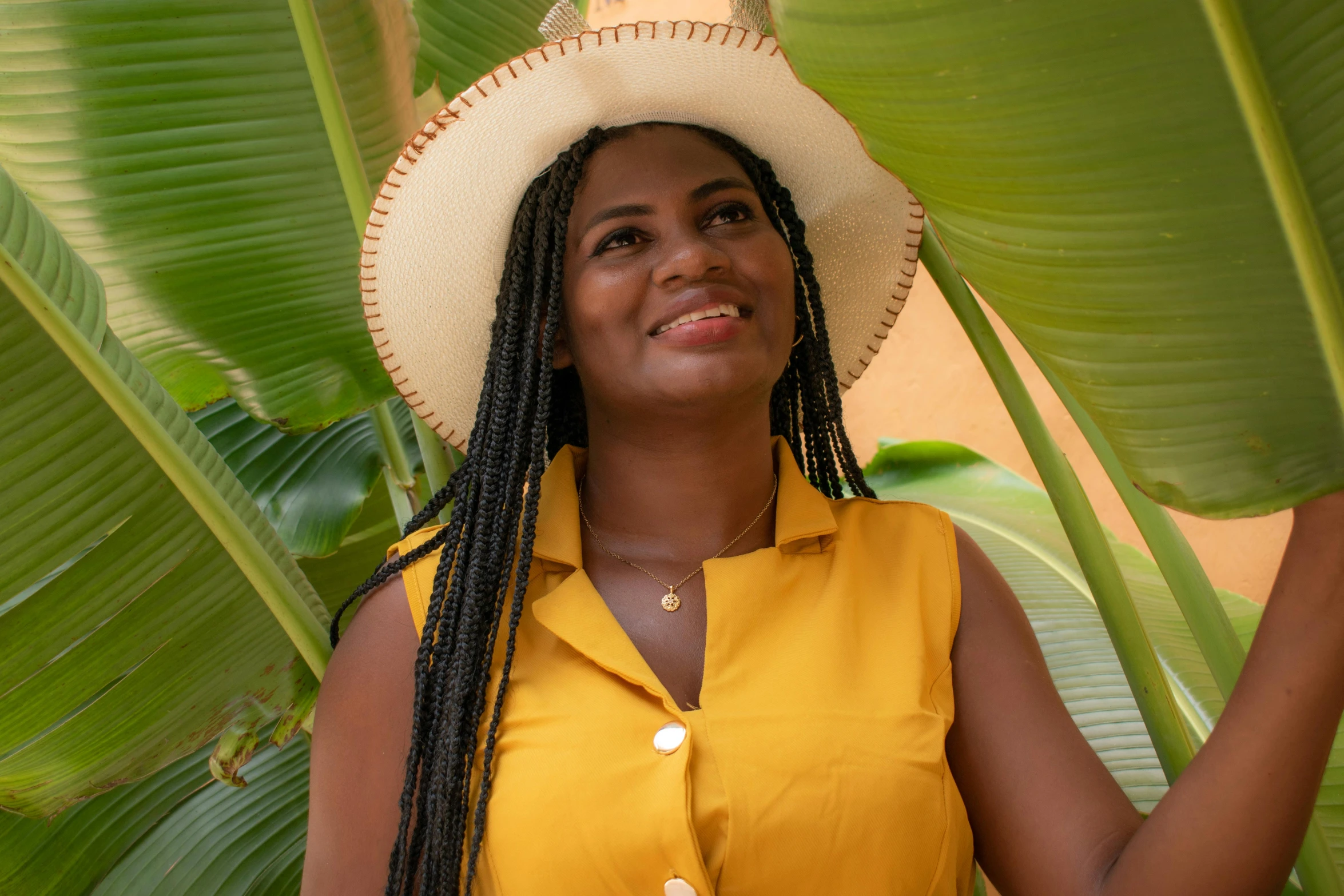 a smiling woman wearing a hat is next to green leaves