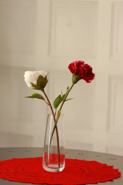 two roses sit in a vase on a red placemat