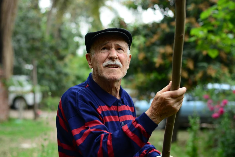 an old man holding a stick and wearing a cap