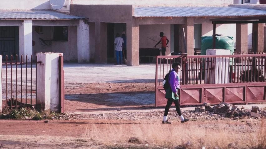 the person walks outside a building past a fence