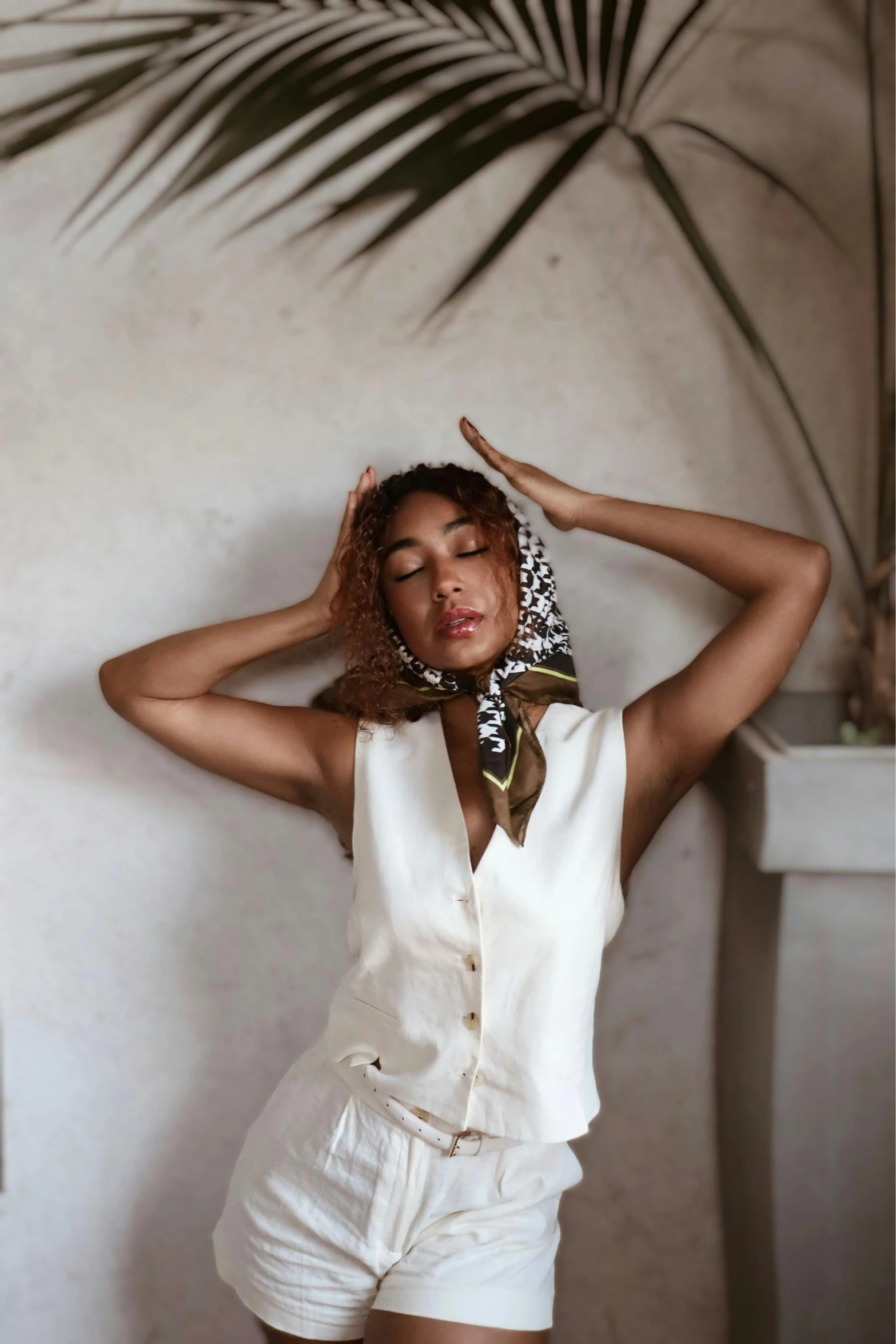 woman in white outfit wearing scarf leaning against wall