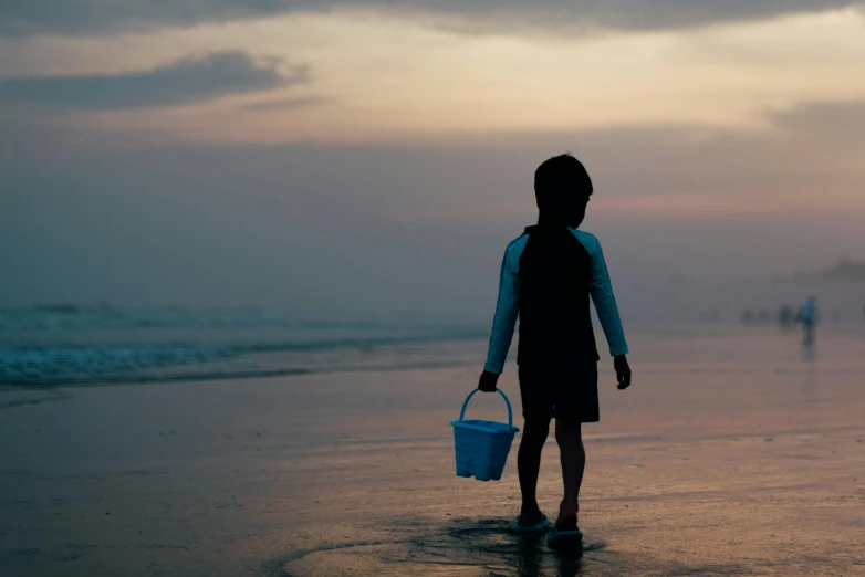 a person walking on a beach with a bucket