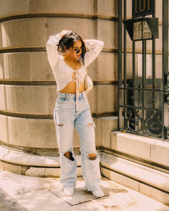 a woman in ripped jeans standing by a wall