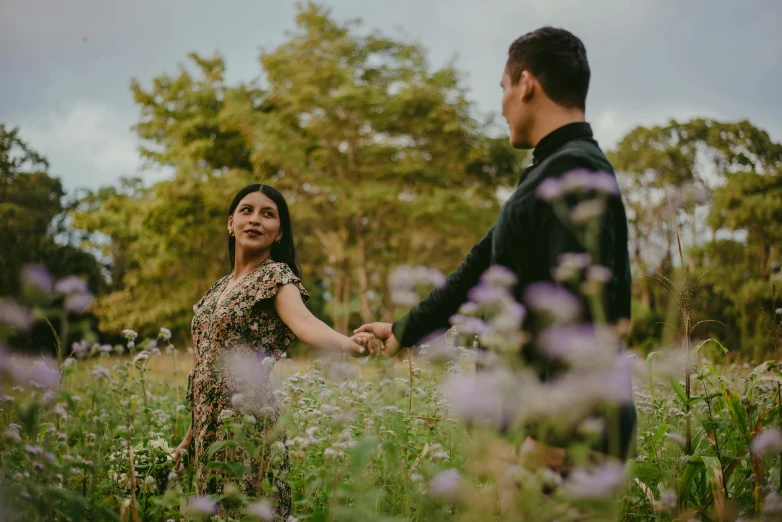 a man and woman hold hands walking through the grass