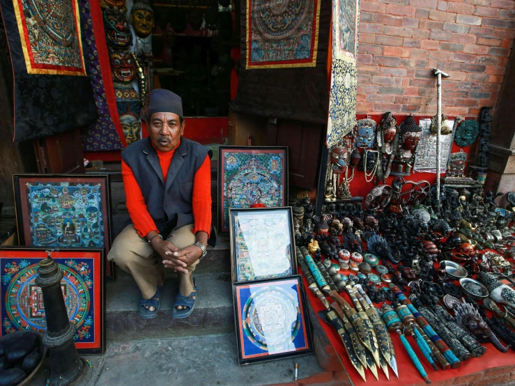 a man squatting down behind the shop selling an array of colorful and artistic items