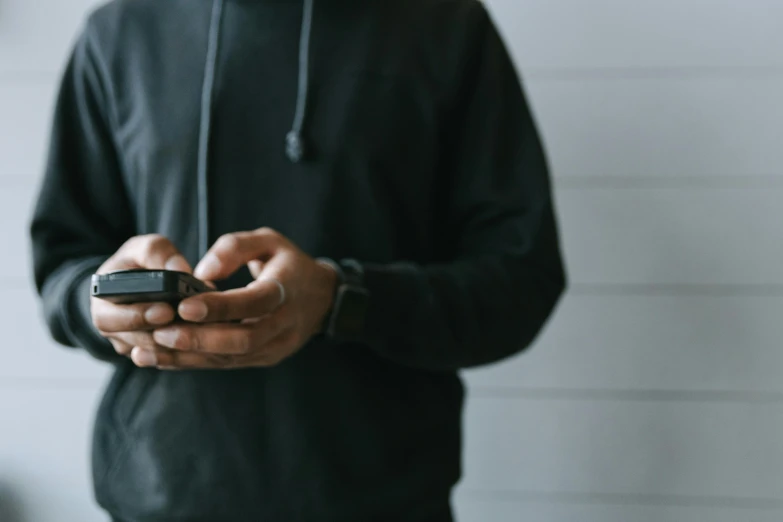 a person standing holding a cell phone while wearing a hoodie