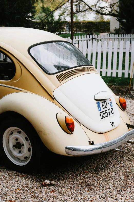 a tan and white vw bug parked in gravel