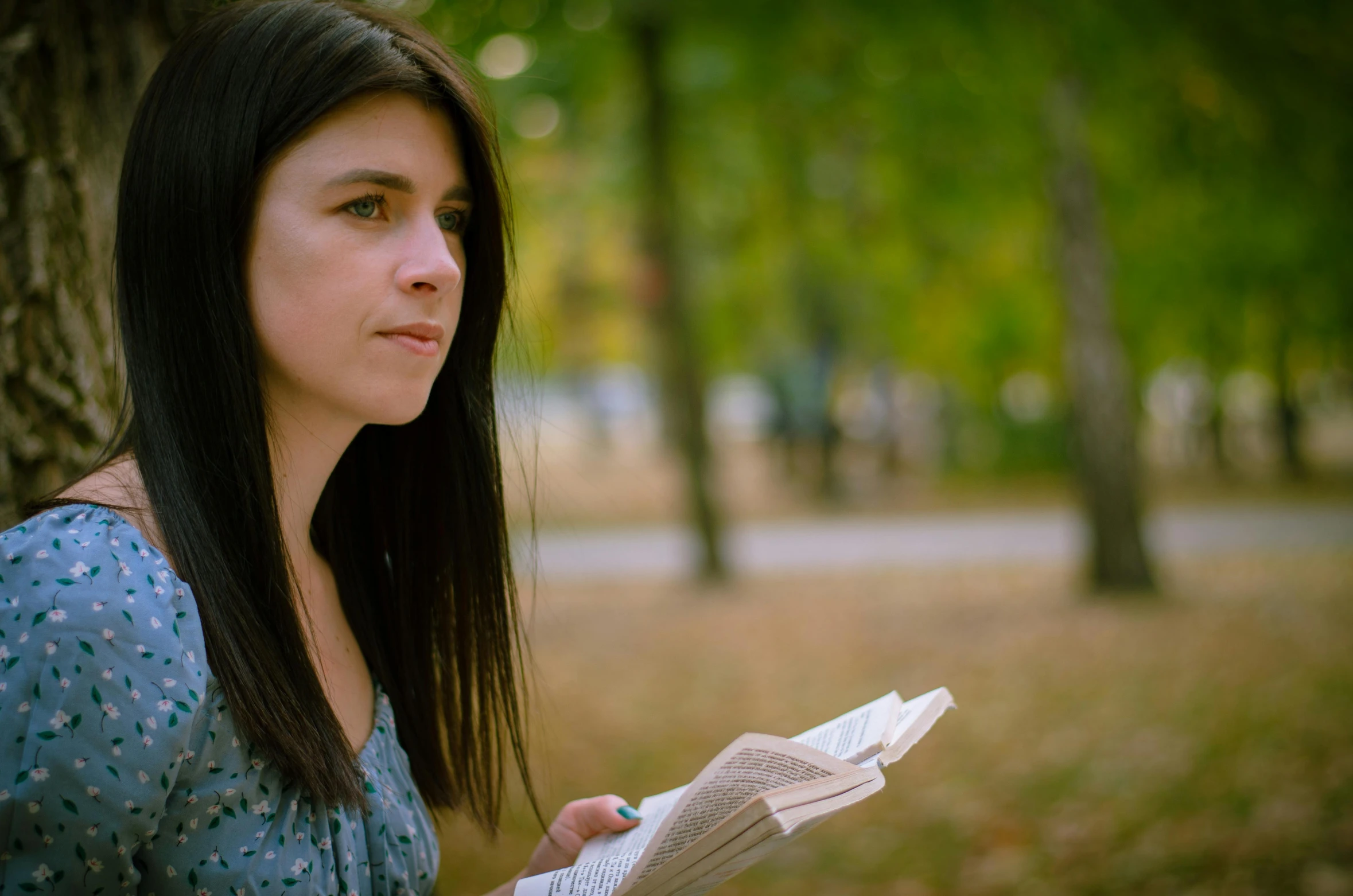 a woman holding a book next to a tree in a park