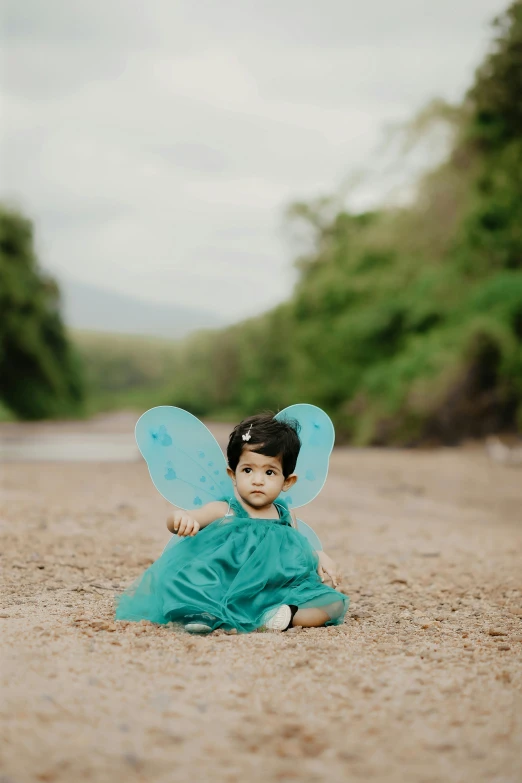 a boy dressed as a fairy sits on the beach