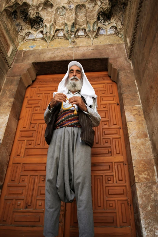 a bearded man in traditional indian garb, standing in front of wooden doors