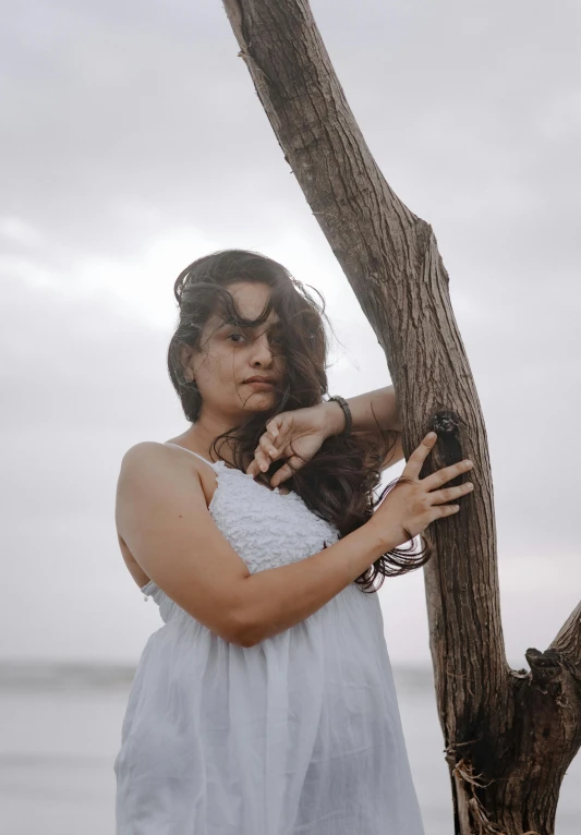 woman in white dress leaning against tree by beach