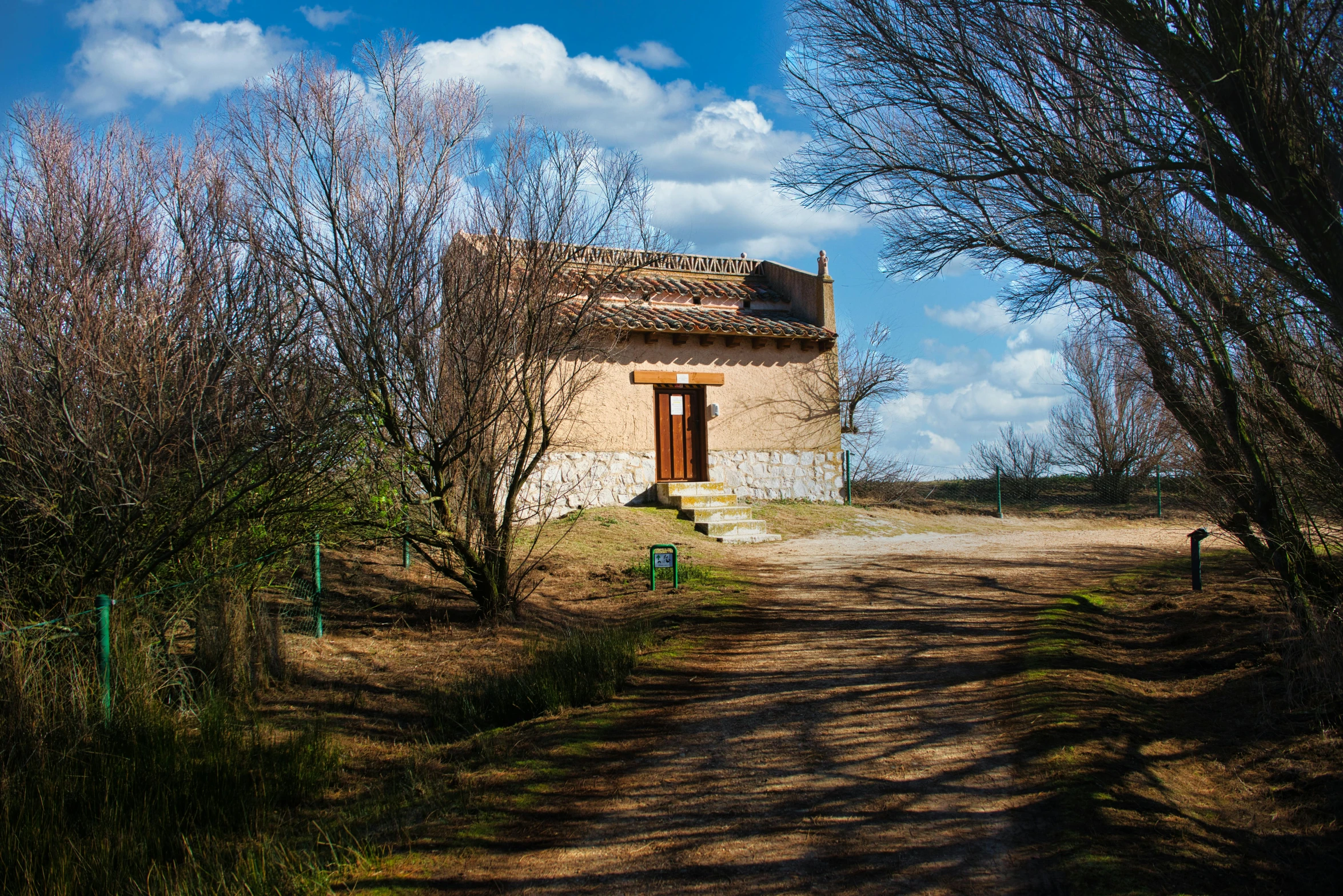 a dirt road running past a small building in the middle of a forest