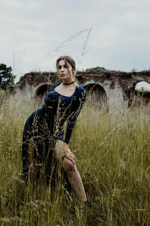 a woman in a blue dress in tall grass near a brick wall