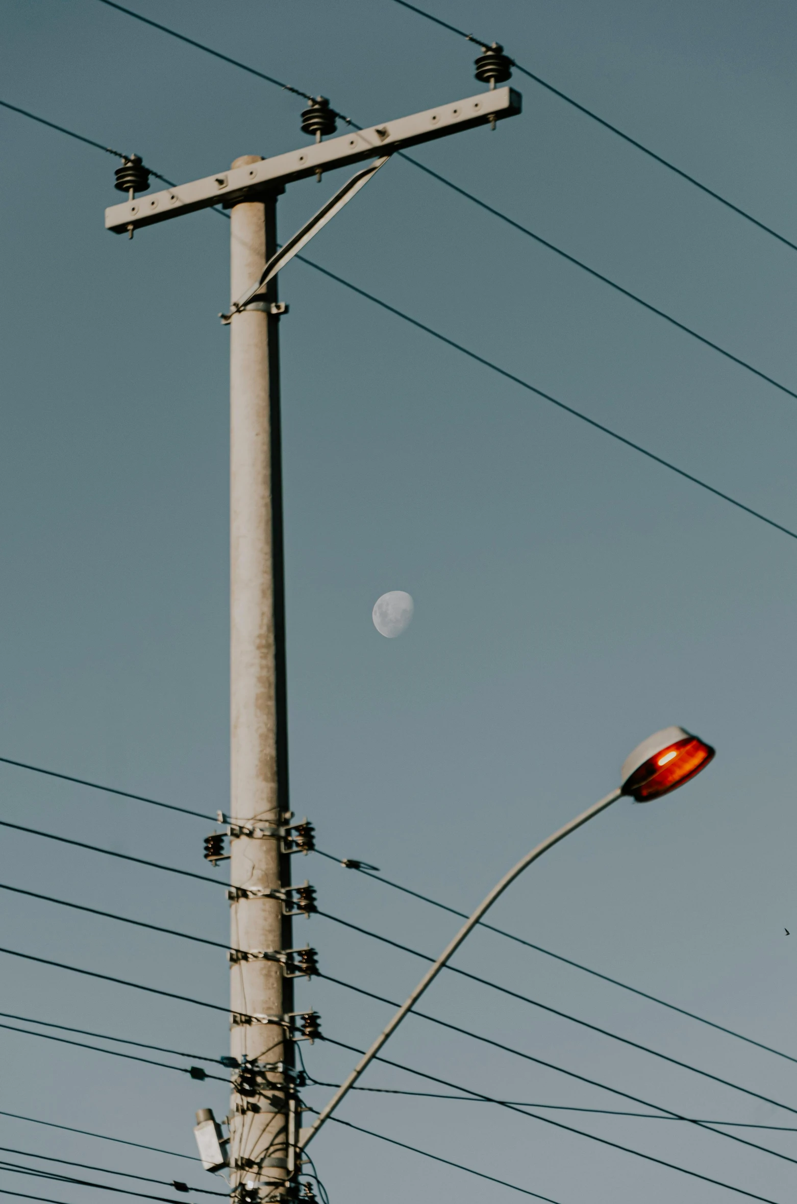 an empty pole with many telephone wires and the moon in the distance