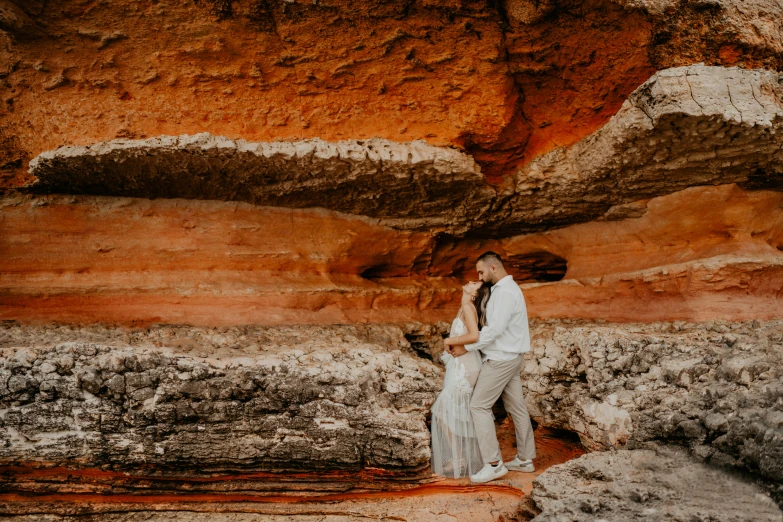 a newly married couple standing next to a large boulder