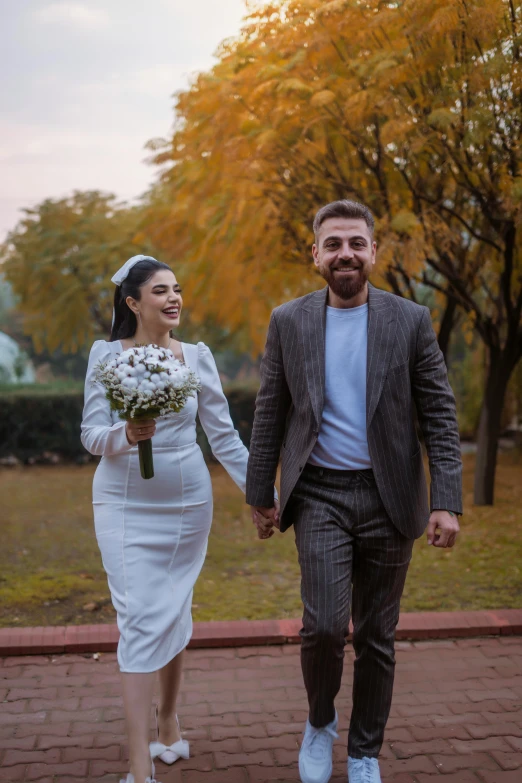 a bride and groom walking down the sidewalk with flowers in hand