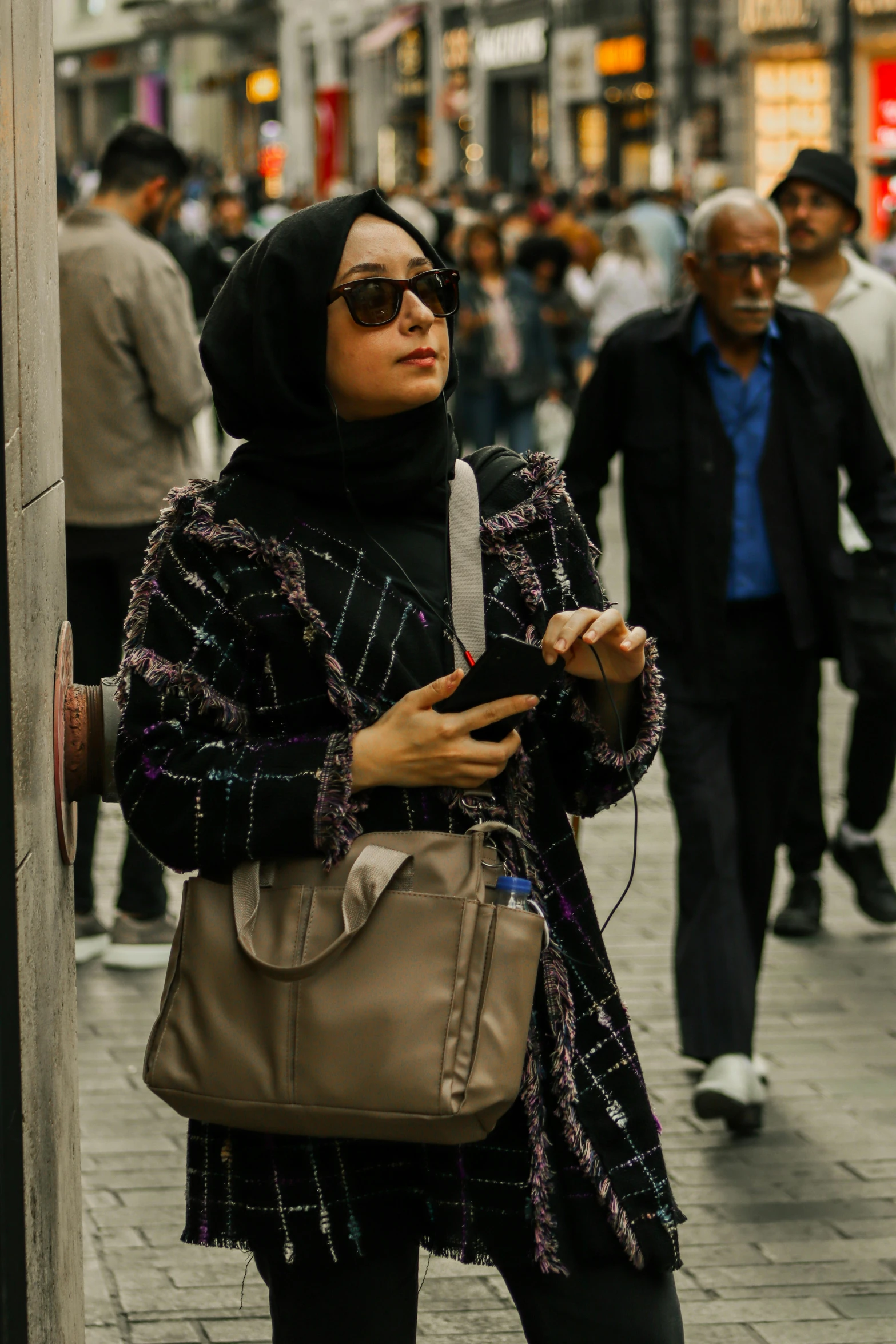 the woman with sunglasses has a purse and cell phone in hand