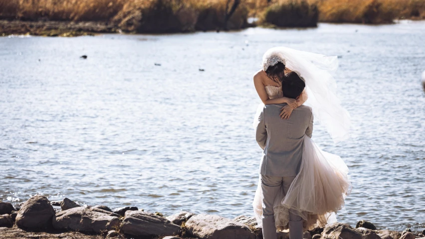 a woman with her arm around a man who is standing in front of water