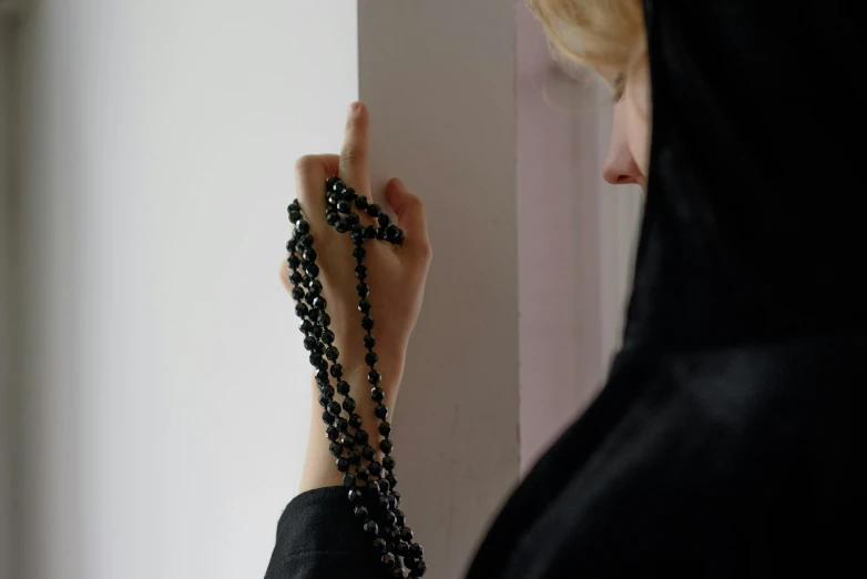 a person looking through a wall with a rosary hanging down