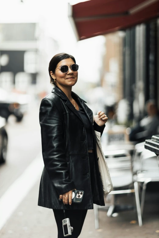 a woman posing on a city sidewalk in a black leather coat