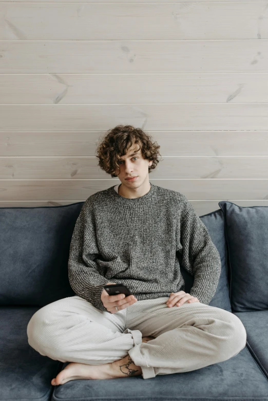 the man is sitting on a blue couch while holding his phone